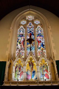 A complex photo of the altar with a triptych in the reredos behind (showing Jesus with the twelve apostles in adoration?) and the east window above. Re the reredos: 'Prior to that [before 1913] a beautiful Caen stone Reredos was erected as a memorial to Archdeacon Watkins at a cost of about £300.' Re the east window: 'The east window is a magnificent work, the three main lights respectively depicting "The Appearance in the Upper Room," "Stilling the Tempest," and "Christ and the Magdalen," and was erected many years ago in memory of Henry Maxwell Lefroy, 1879; Thomas Brown, 1863; and Daniel Scott, 1865.' The Western Mail, Friday 27 May 1914, p. 34.